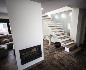 Interior de un salón con chimenea encastrada en una columna y escaleras al fondo, de estilo nórdico.